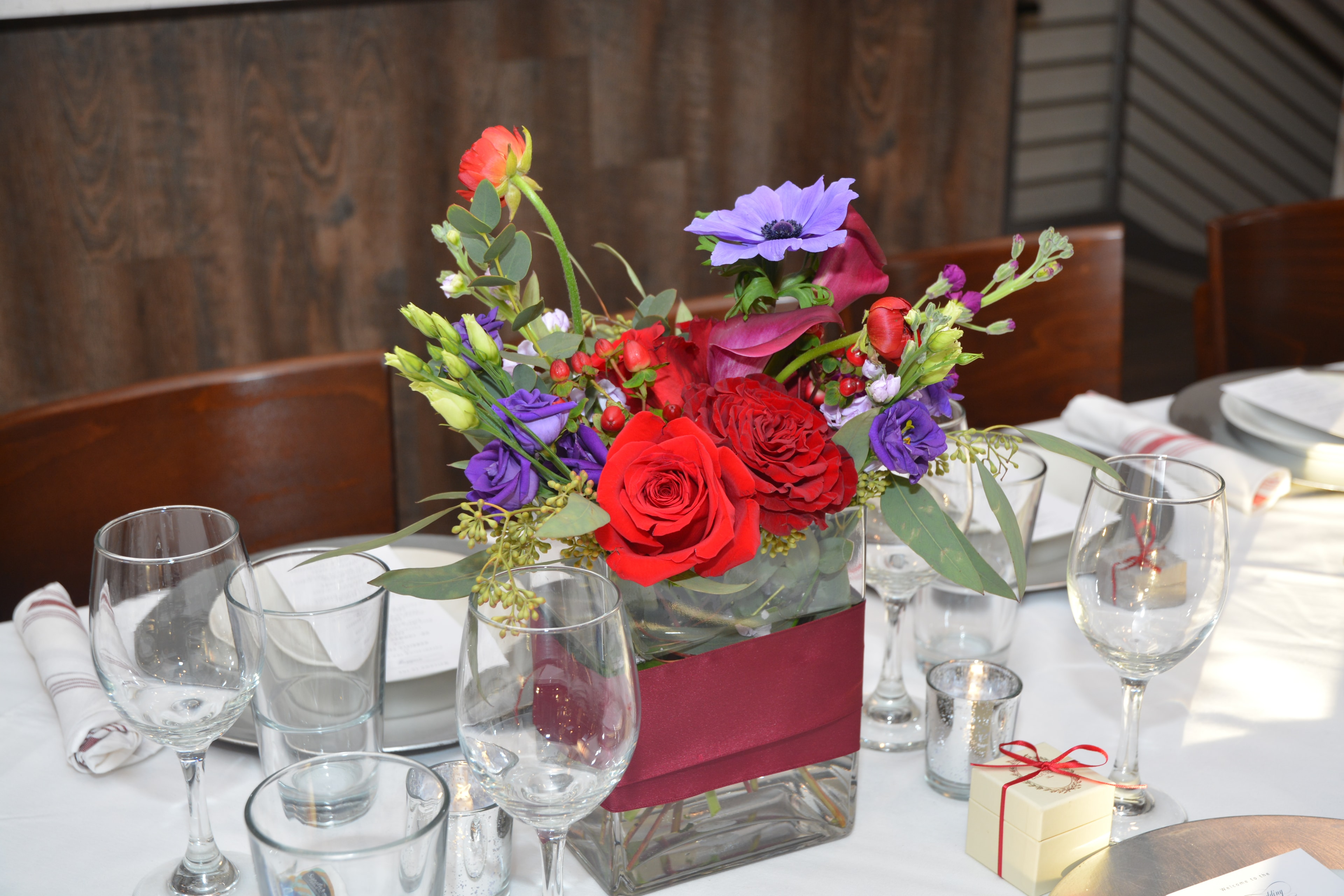 Floral centerpiece with red roses and purple flowers at a wedding reception table