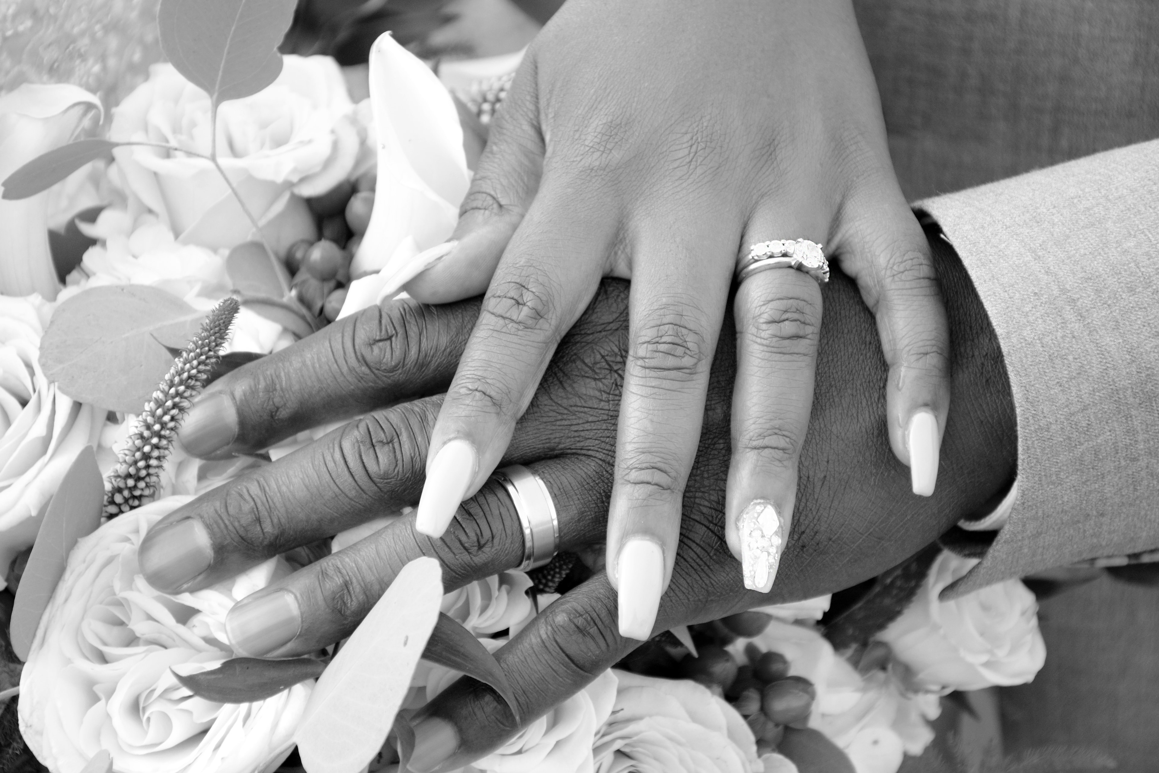 Black and white close-up of bride and groom's hands showing wedding rings