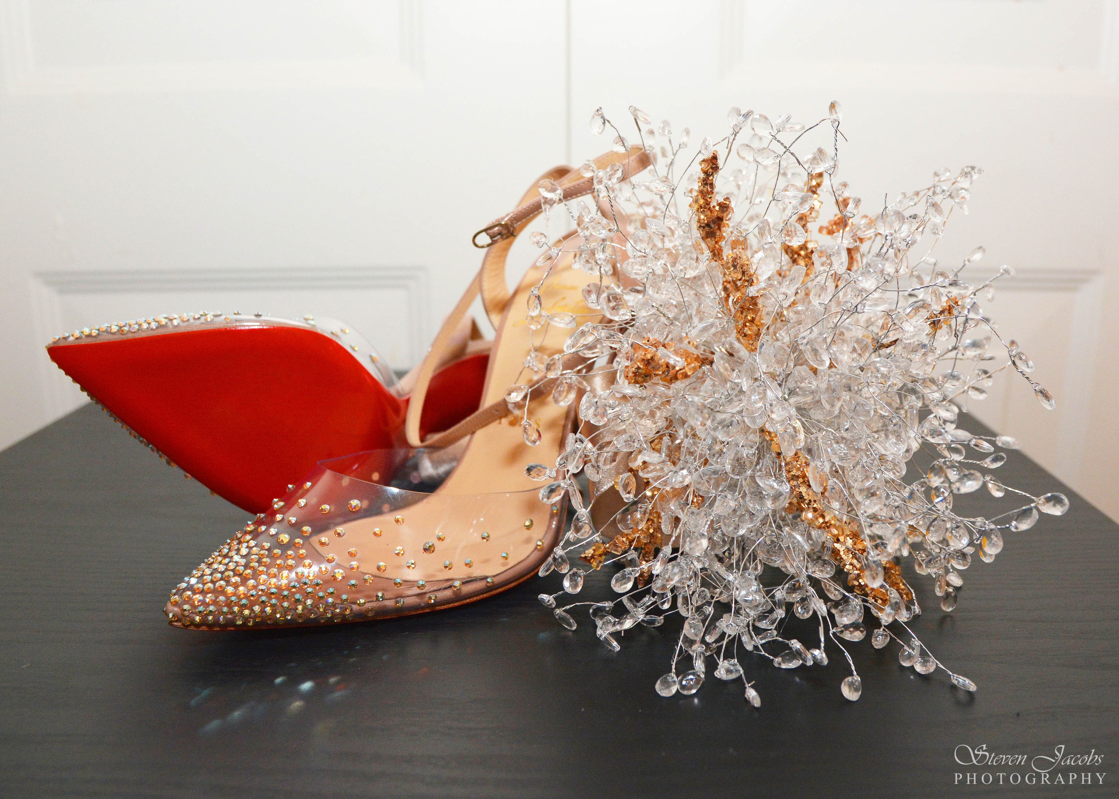 Crystal-embellished bridal heels with red soles beside a sparkling bouquet